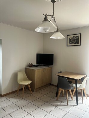 Een ruime, goed verlichte kamer met een eettafel, twee stoelen, een televisie op een houten kast en een plafondventilator.