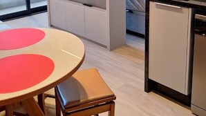 Ett modernt hotellrum med en säng, en TV, en matplats med bord och stolar samt ett litet kök.