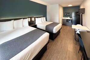 Et hotelværelse med to senge, et skrivebord, en stol, et tekøkken og et fjernsyn.