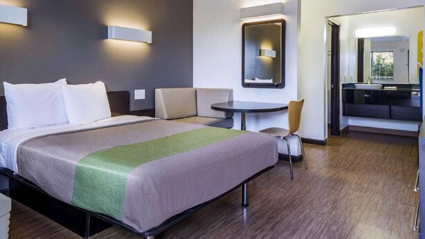 Ein Hotelzimmer mit einem Bett, einem runden Tisch, einem Sessel, einem Spiegel und einem durchgegangenen Tür sichtbaren Badezimmer.