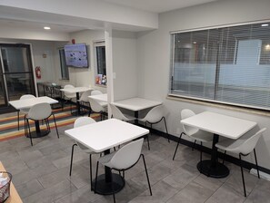 A modern dining area with white tables and chairs, a fire extinguisher, and a window with blinds. - Ideal for Long Vacations & Rock Springs Stays | Rock Springs Arch - 2.2 miles (Rock Springs)