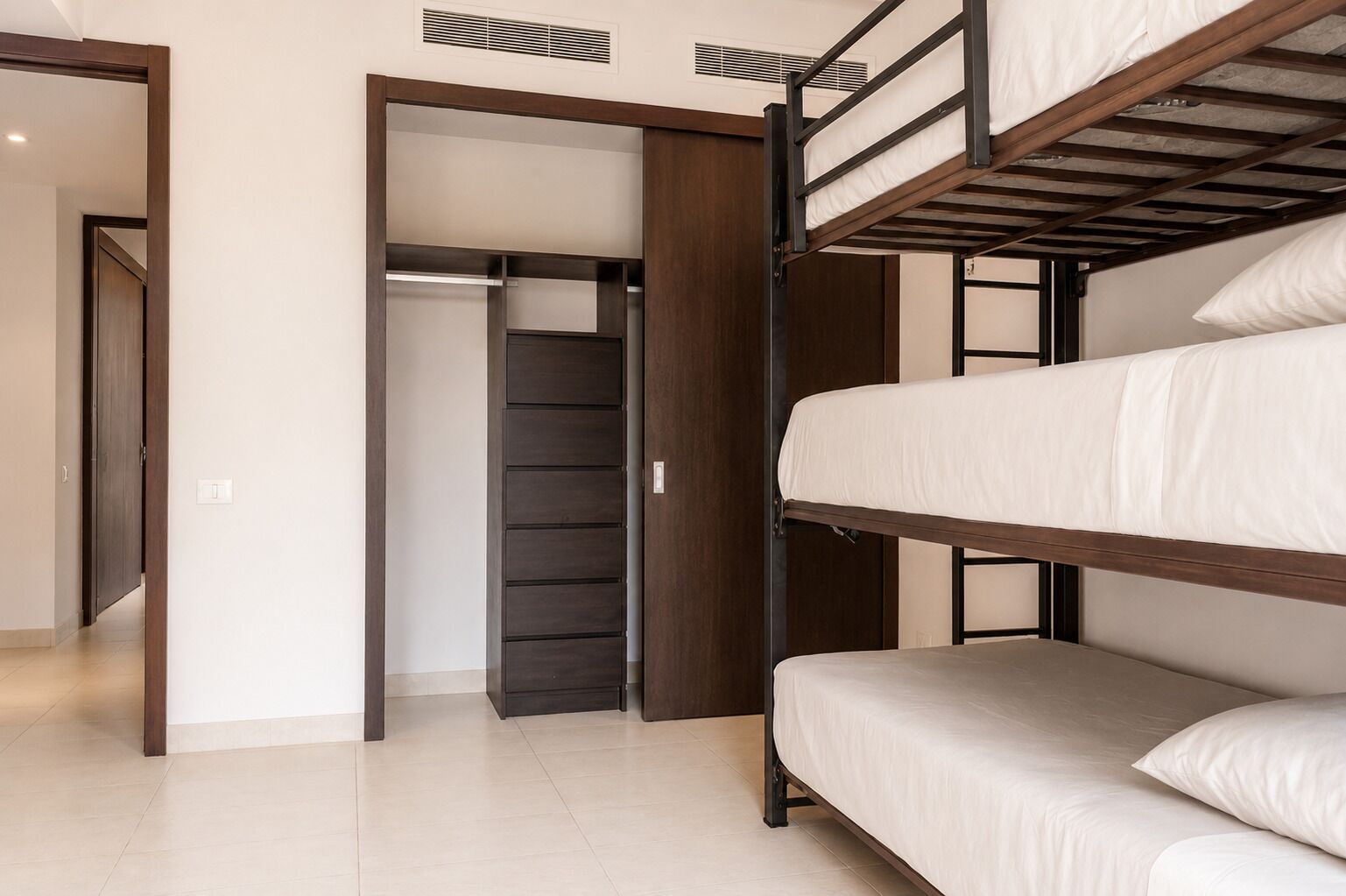 Habitación con literas, un armario y una puerta que da a otra habitación.