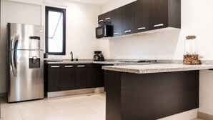 Eine moderne Küche mit dunklen Schränken, einem Edelstahlkühlschrank, einer Mikrowelle und einer Arbeitsplatte aus Granit.