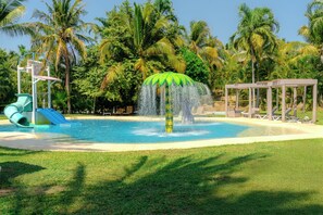 Ein Wasserpark mit Rutsche, Wasserspeier und Liegestühlen.