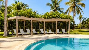 A pool area with lounge chairs and a covered seating area, surrounded by palm trees.