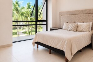 Un dormitorio con cama, una mesita de noche y vistas a palmeras a través de amplias ventanas.
