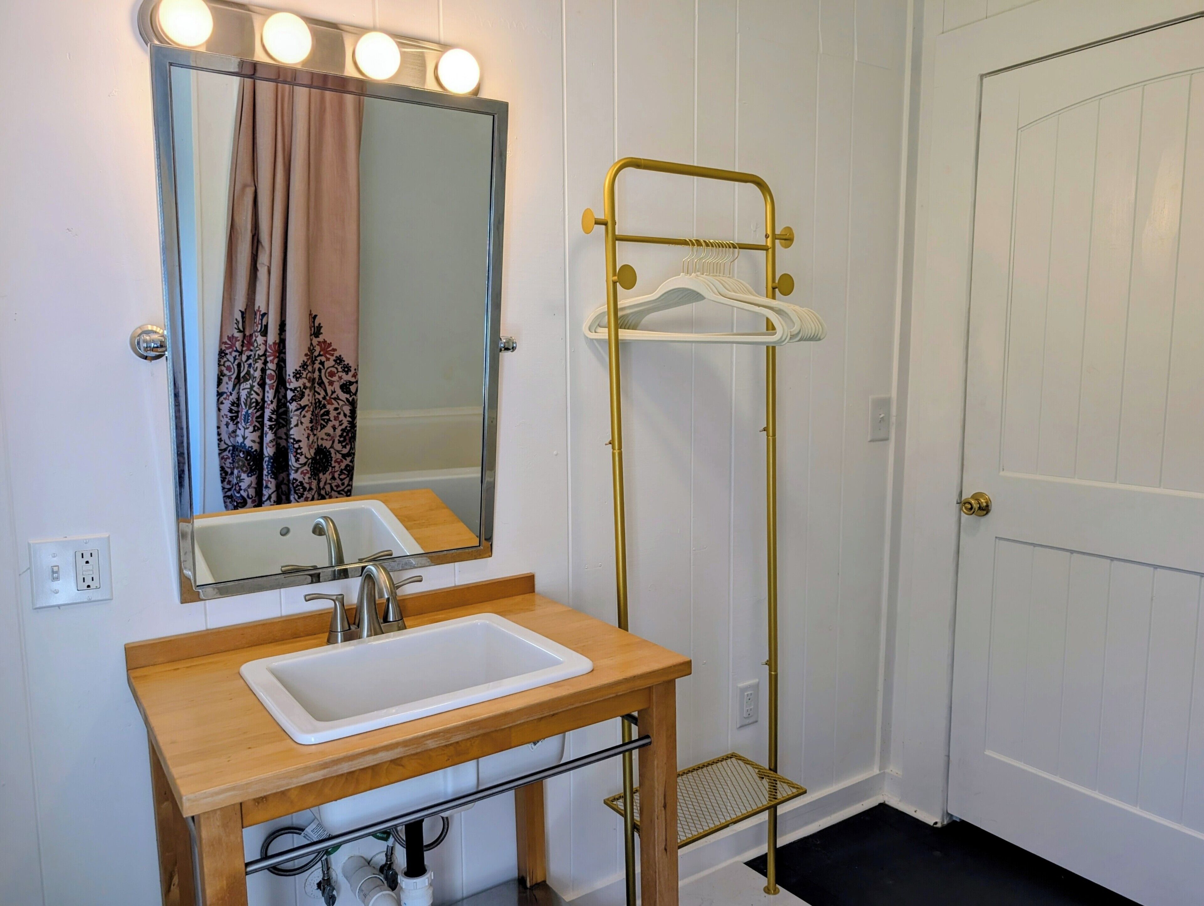 A bathroom with a sink, mirror, vanity, towel rack, and a door.