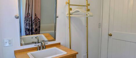 A bathroom with a sink, mirror, vanity, towel rack, and a door.