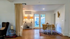 Um quarto com piso de madeira, uma mesa de jantar com cadeiras, uma estante de livros e uma janela com cortinas.