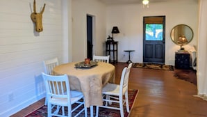 Uma sala de jantar com uma mesa redonda, cadeiras brancas, uma decoração com cabeça de cavalo e uma porta que dá para outro cômodo.