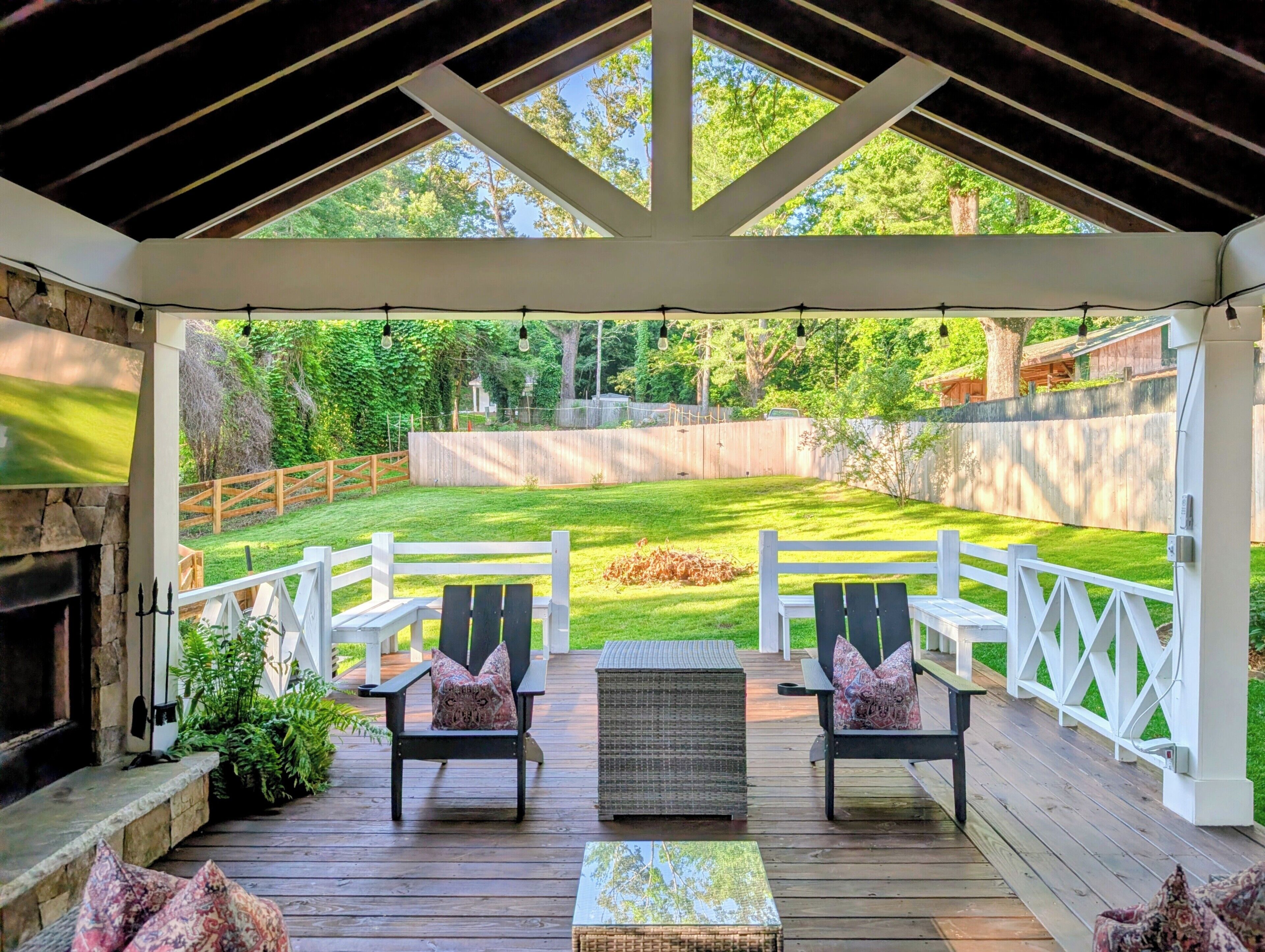 Eine überdachte Terrasse mit zwei Stühlen und einem Tisch, mit Blick auf einen Rasen mit Holzzaun.
