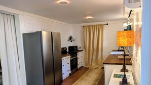 Cozinha compacta com geladeira, fogão, micro-ondas e uma pequena área de refeições com mesa e luminária.