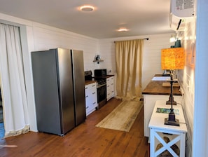 Cocina compacta equipada con refrigerador, estufa, microondas y un pequeño comedor con mesa y lámpara.