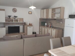 A compact living space with a sofa, dining table, kitchenette, and a television. - Two Bedroom Apartment with Balcony and Garden View (Karlobag)