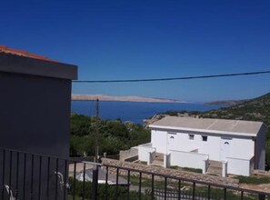 A white building with a flat roof, a stone wall, and a metal railing in the foreground. - Two Bedroom Apartment with Balcony and Garden View (Karlobag)