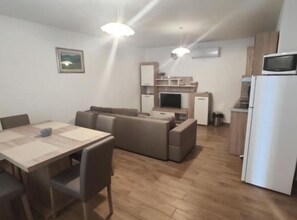 Ein modernes Wohnzimmer mit Esstisch, Sofas, Fernseher und Küchenzeile mit Mikrowelle und Kühlschrank.