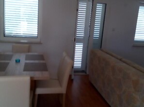 A room with a dining table, chairs, a sofa, and a window with blinds. - Two Bedroom Apartment with Balcony and Sea View (Karlobag)