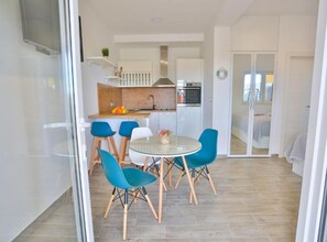 Eine moderne Küche mit weißen Schränken, einem eingebauten Backofen und einem Essbereich mit einem Glastisch und blauen Stühlen.