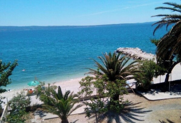 A beach view with clear blue water, a sandy shore, and palm trees. - One Bedroom Apartment with Sea View and Balcony (Podstrana)