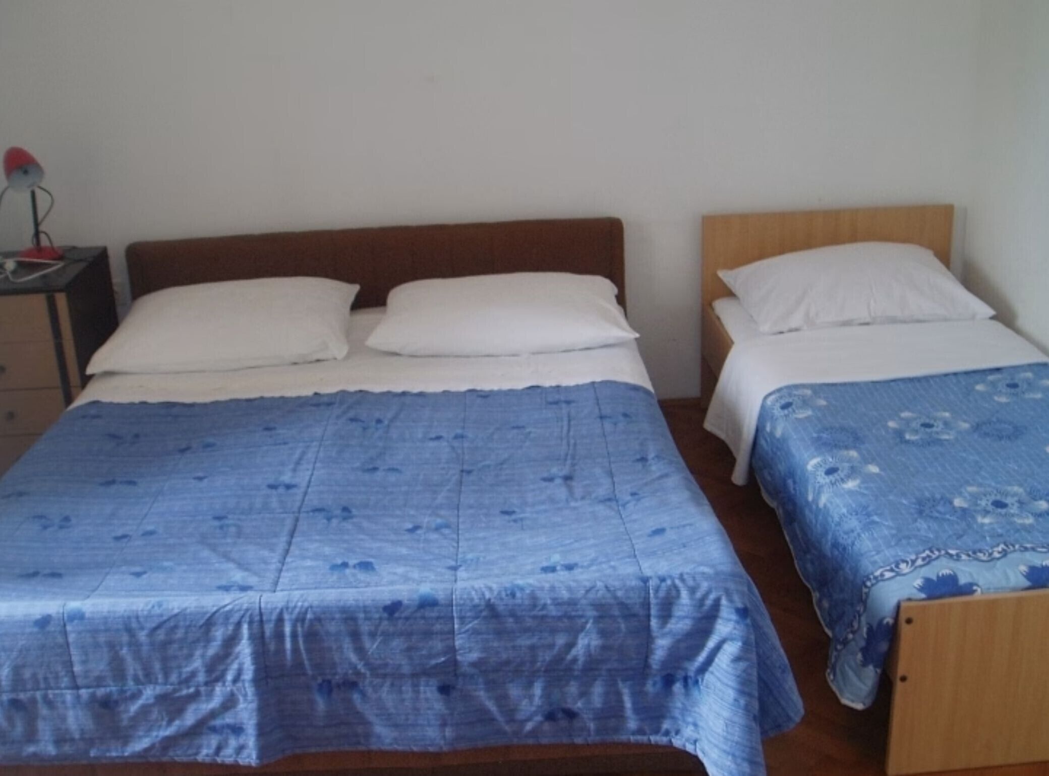 Une chambre avec deux lits, chacun doté d’une tête de lit en bois, d’une table de chevet avec une lampe et d’une commode.