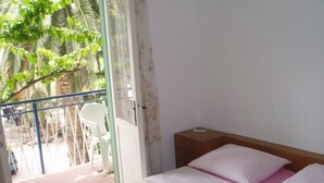 A bedroom with a bed, a nightstand, a window, and a view of a balcony with a chair.