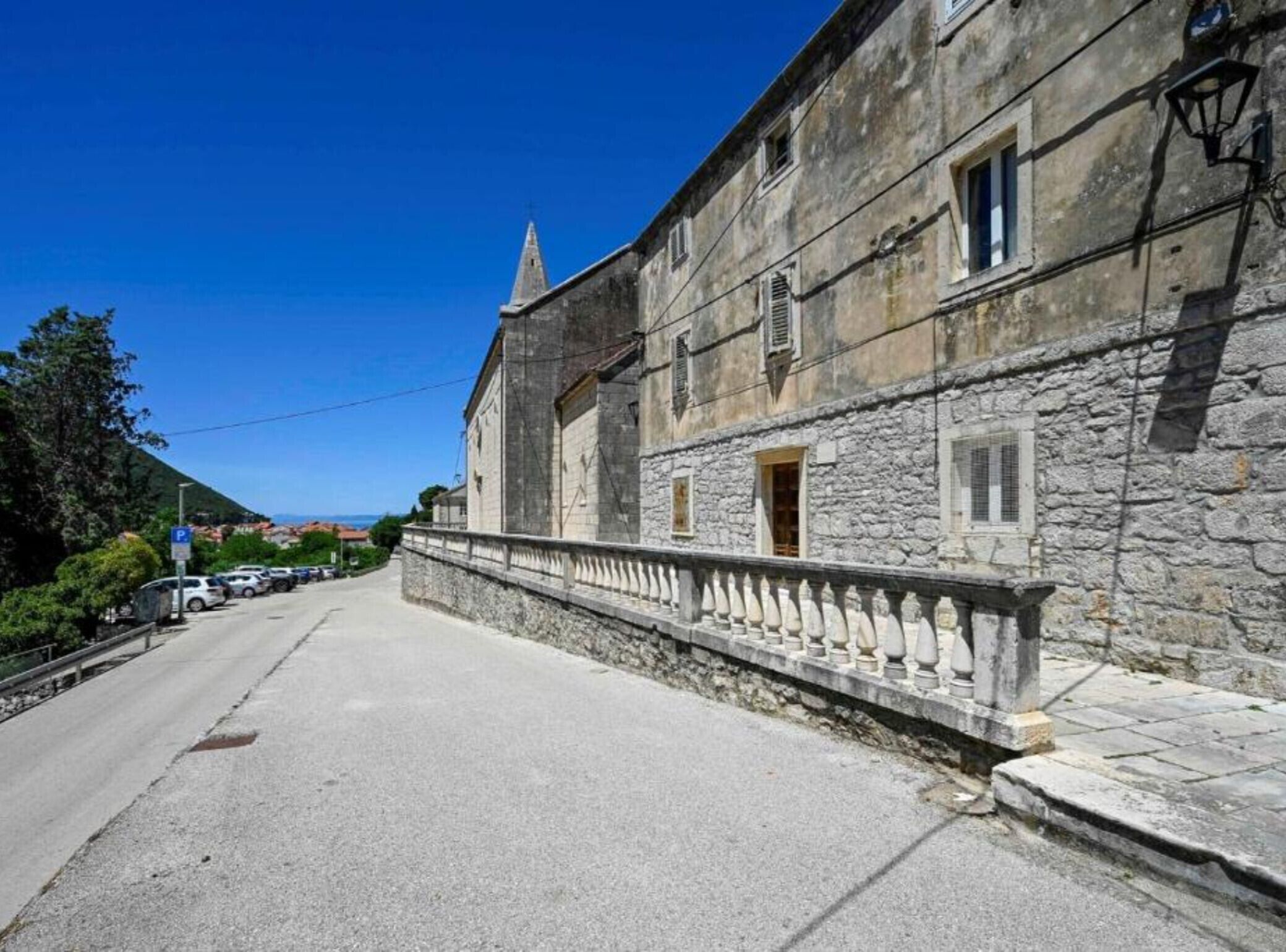 A stone building with a balcony, a clear sky, and parked cars along the street.