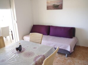 Ein Zimmer mit einem Bett, einem Tisch mit Tischdecke und einem Gemälde einer Strandansicht.
