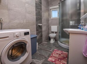 Ein kleines Badezimmer mit Waschmaschine, Toilette und Dusche.