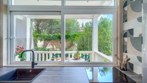 Eine Küche mit Fenster, Spüle und Blick auf einen Balkon mit Pflanzen und Gartenmöbeln.