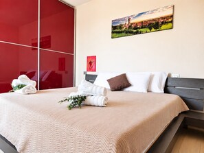 Ein modernes Hotelzimmer mit einem großen Bett, einem roten Wandschrank und einem Stadtbild an der Wand.