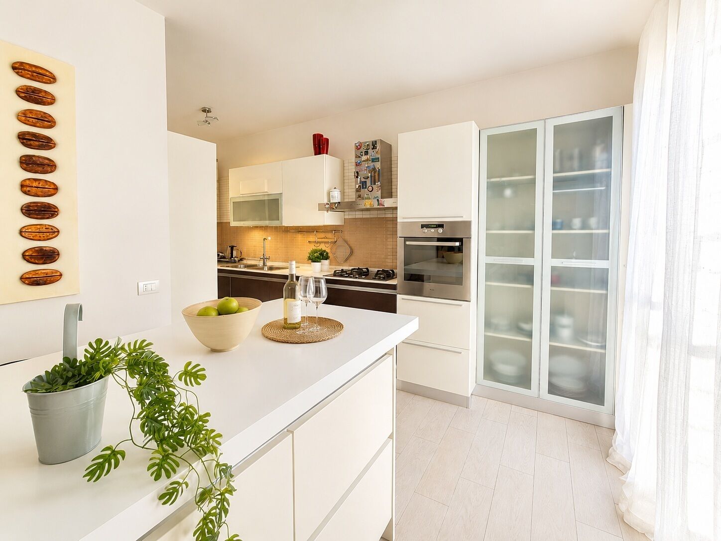 A modern kitchen with white cabinets, a central island, and a glass-fronted pantry.