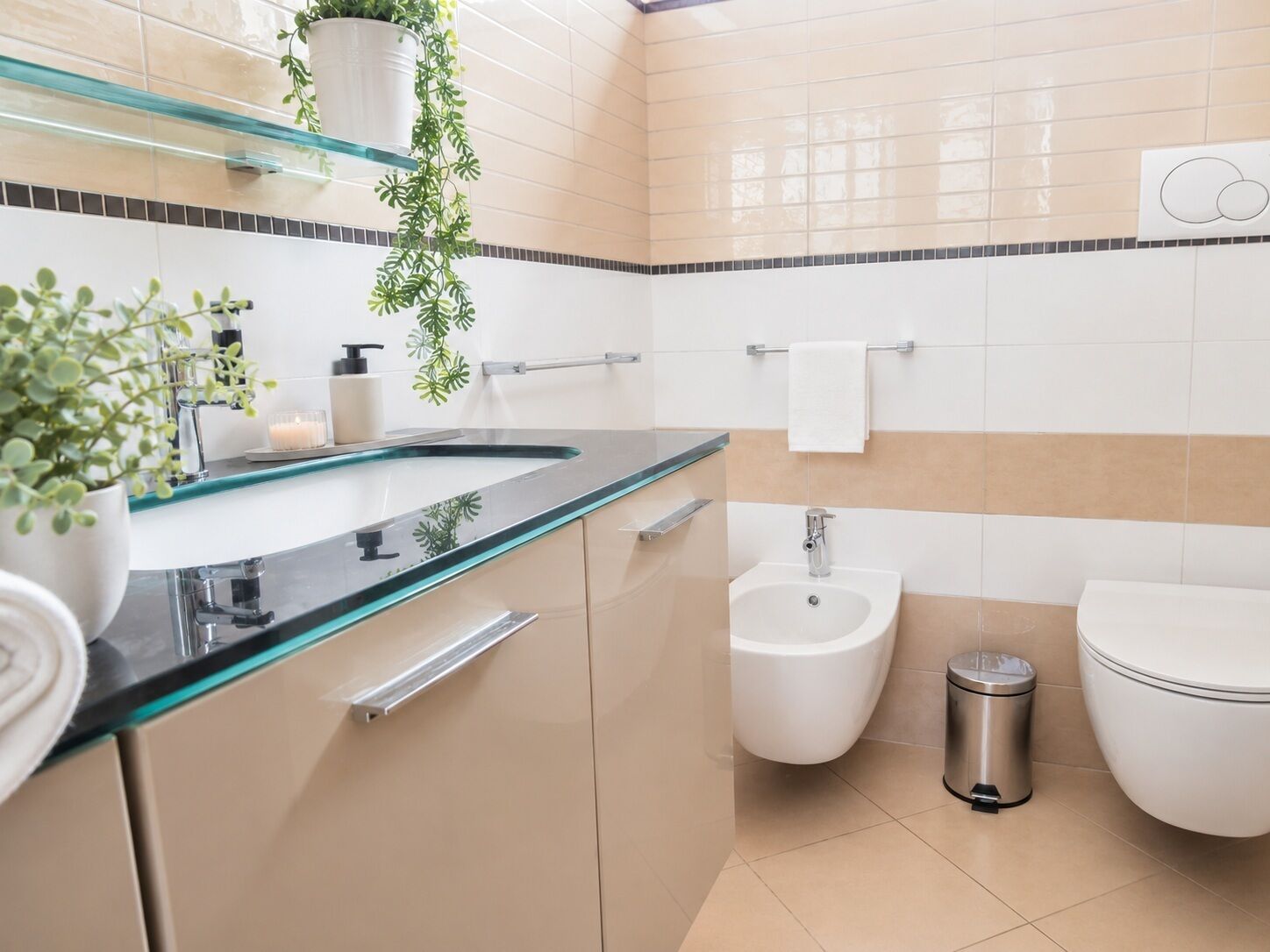 A modern bathroom with a glass sink, a bidet, a toilet, and a trash bin.