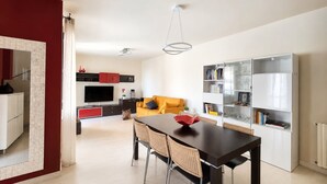 Um espaço de estar moderno com área de jantar, sofá, TV e estante.