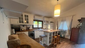 Une cuisine compacte avec des meubles blancs, un lave-linge, un évier et un coin bar avec des tabourets.