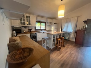 A compact kitchen with white cabinets, a washing machine, a sink, and a bar stool area.