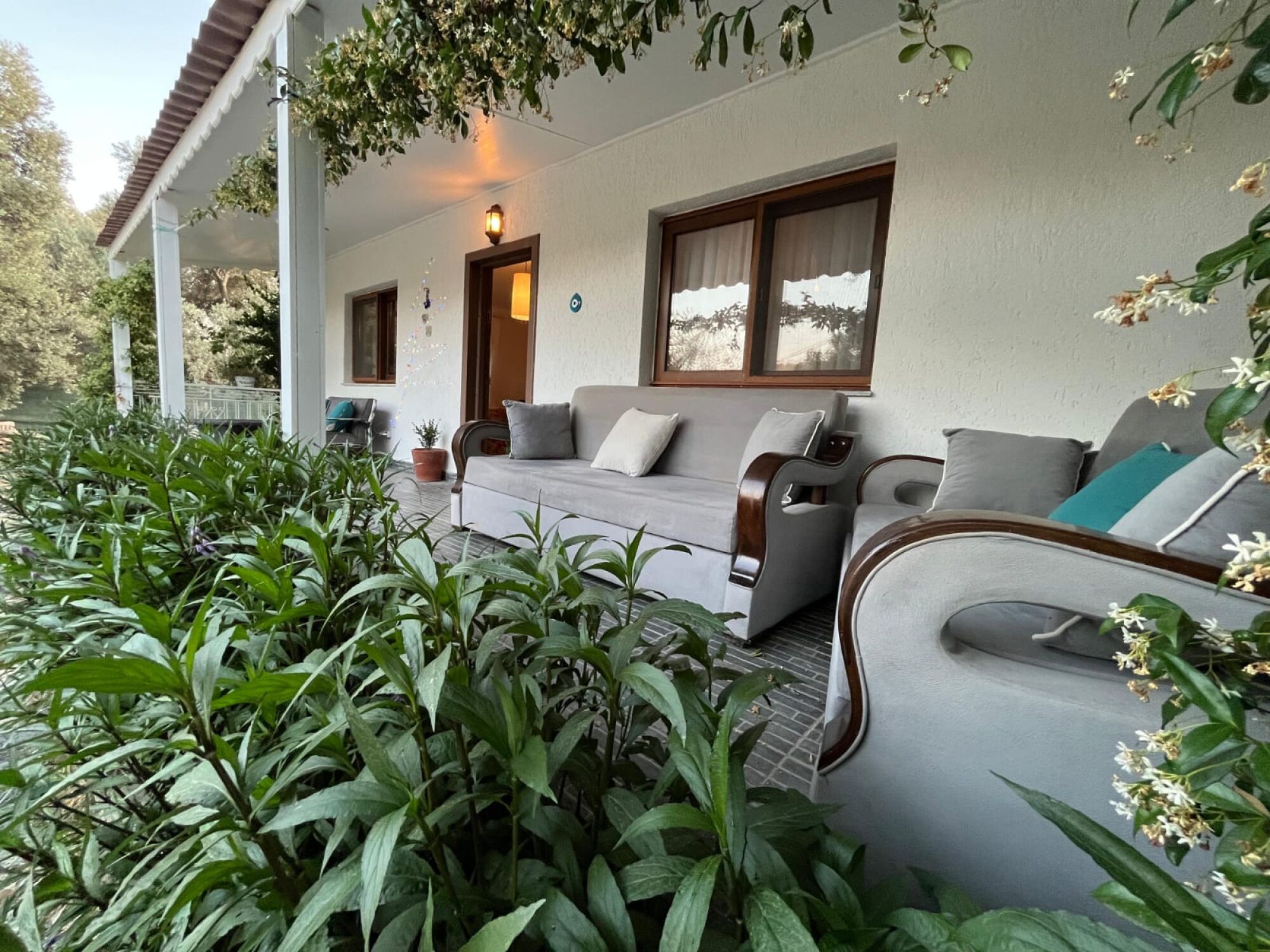 Un espace extérieur aménagé, abrité et doté d’un canapé et de fauteuils, le tout entouré de verdure.