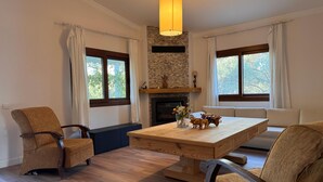 Une pièce avec une cheminée, une table à manger et deux fenêtres avec des rideaux.