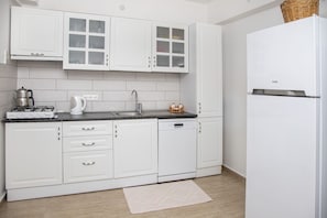 Eine moderne Küche mit weißen Schränken, einem Gasherd, einem integrierten Geschirrspüler und einem weißen Kühlschrank.