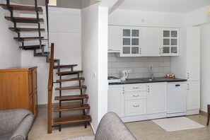 Eine Küche mit weißen Schränken, einer Holztreppe und einem grauen Sofa.