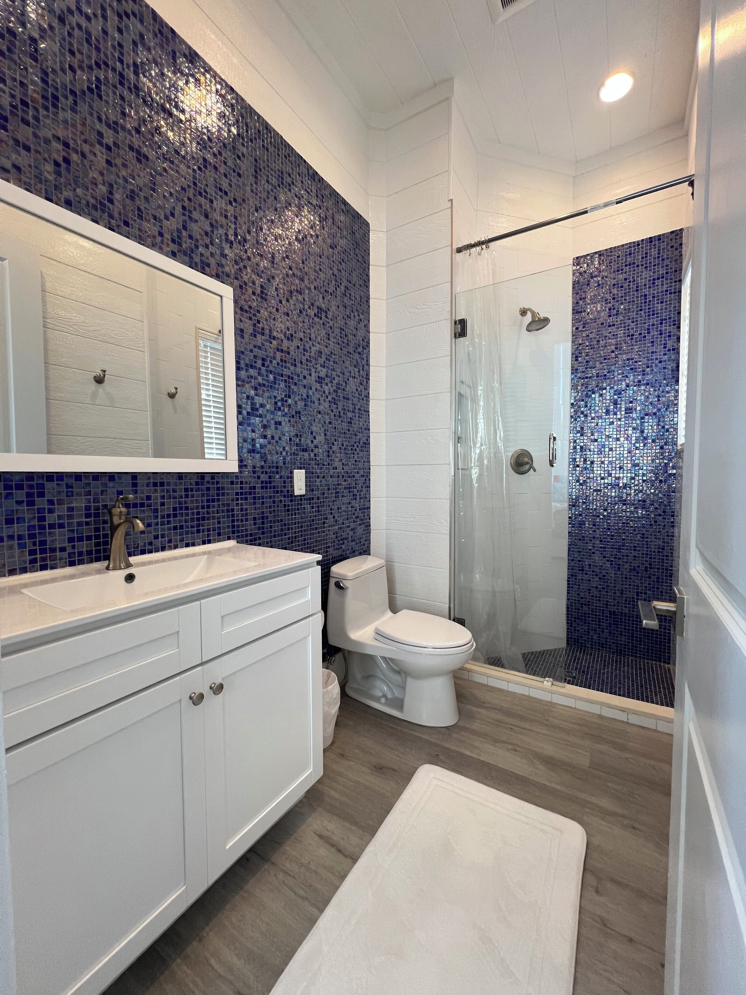 Une salle de bain avec un meuble-lavabo blanc, des toilettes et une douche aux carreaux de mosaïque bleus.