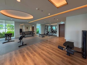 Ein großzügiger Fitnessraum mit unterschiedlichen Trainingsgeräten, großen Fenstern und Holzboden.
