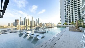 A rooftop pool with a city skyline view, lounge chairs, and a high-rise building in the background. - Aesthetic 1 Bed l Overlooking Marina City Skyline (Dubai)