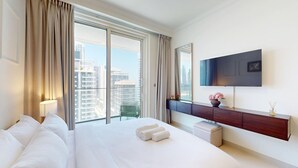 A hotel room with a large bed, a TV mounted on the wall, a balcony with curtains, and a view of high-rise buildings. - Aesthetic 1 Bed l Overlooking Marina City Skyline (Dubai)