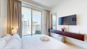Ein Hotelzimmer mit einem großen Bett, einem an der Wand befestigten Fernseher, einem Balkon mit Vorhängen und Blick auf hohe Gebäude.
