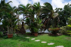 A garden with palm trees, a stone pathway, and a body of water. - Dolce Vita Villa Moorea (Moorea-Maiao)