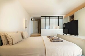Ein Hotelzimmer mit Bett, Fernseher, Schreibtisch und begehbarem Kleiderschrank.
