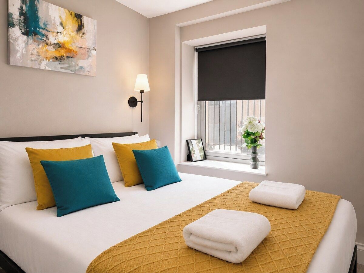 A hotel room with a bed, pillows, a window with a view, and a painting on the wall.