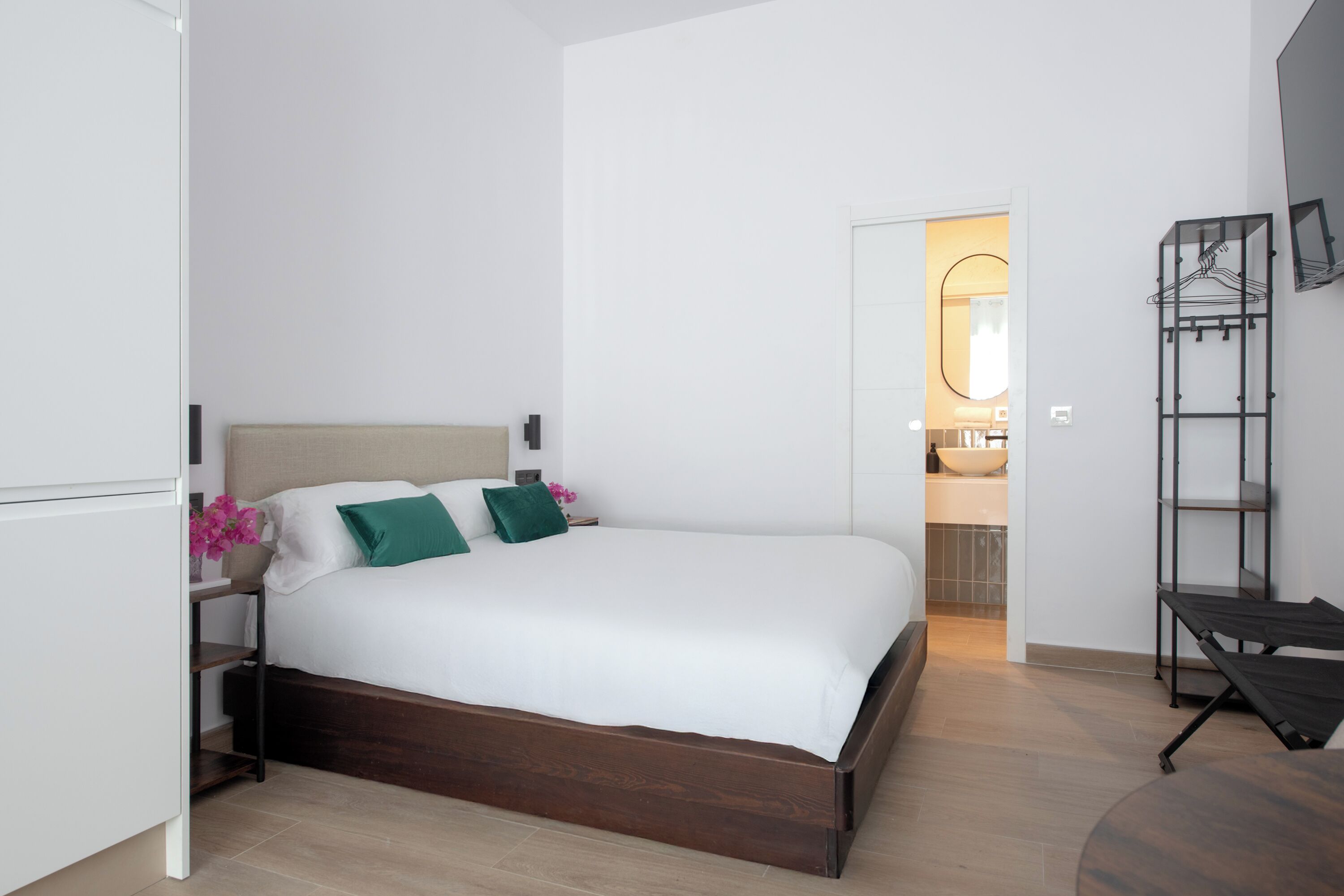 A modern bedroom with a wooden bed frame, white bedding, and a nightstand with a vase of flowers.