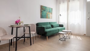 Een moderne woonkamer met een groene bank, een eettafel met stoelen, een klein bijzettafeltje en een schilderij aan de muur.