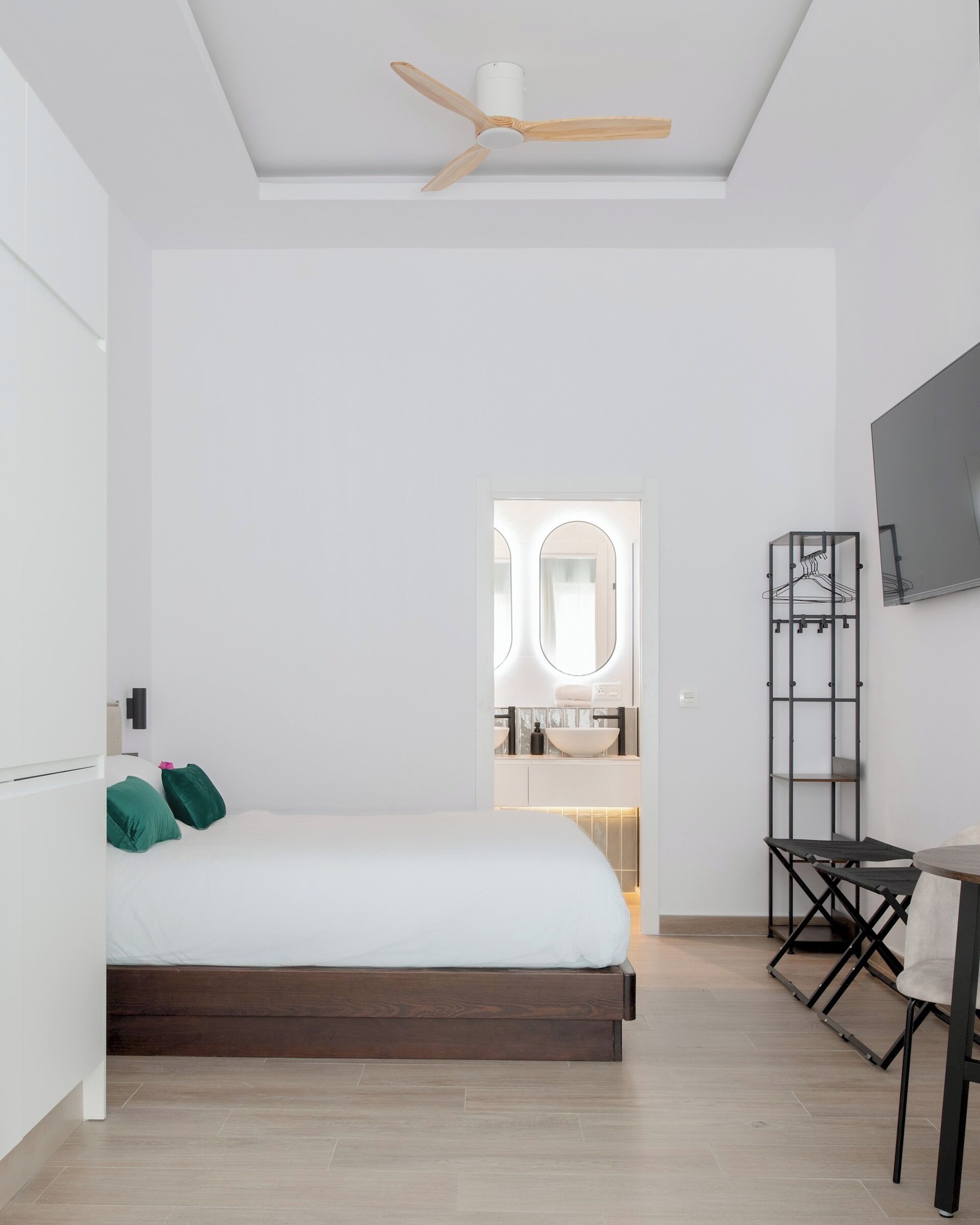 A bedroom with a bed, a ceiling fan, a mirror, a TV, and a desk.